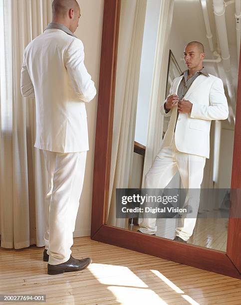 young man adjusting suit jacket in full length mirror - modischer anzug stock-fotos und bilder