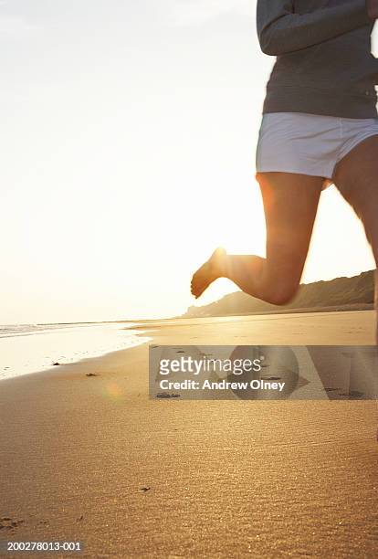 bare footed woman running along beach, low section (sun flare) - bare footprints stock-fotos und bilder