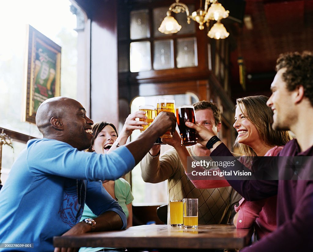 Group of friends around pub table, toasting drinks, smiling, side view