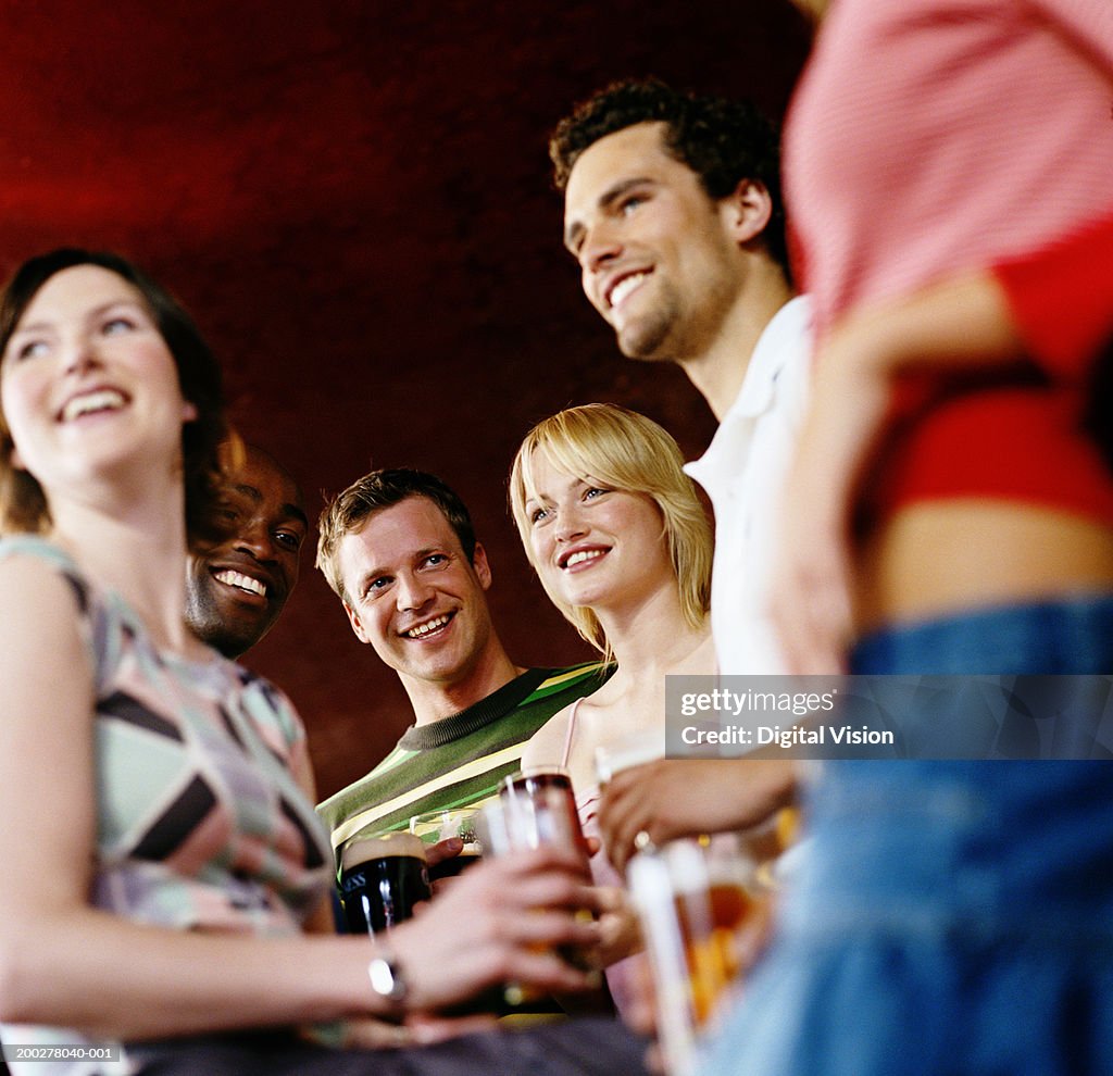 Group of friends in pub holding drinks, smiling, low angle view