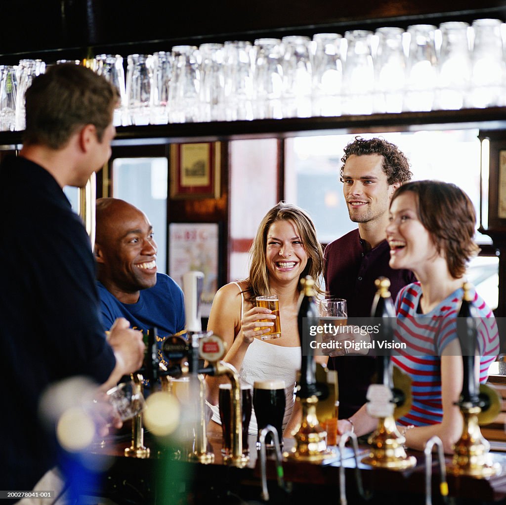 Group of friends at bar talking to barman, smiling