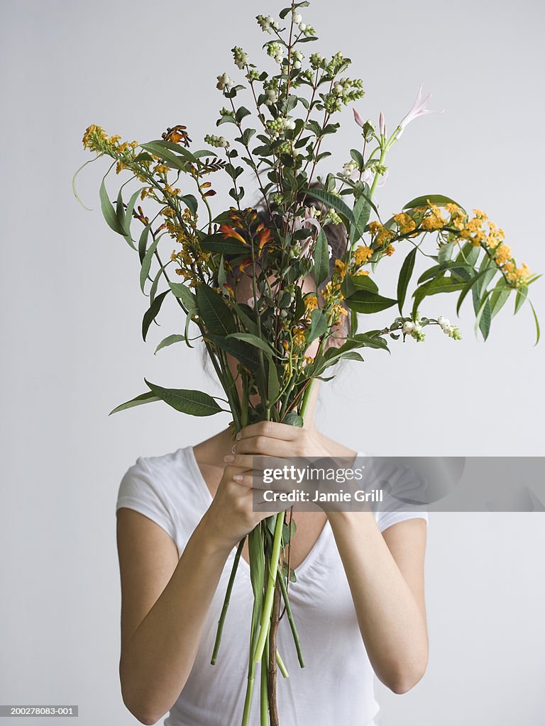 Woman holding wildflowers and weeds in front of face