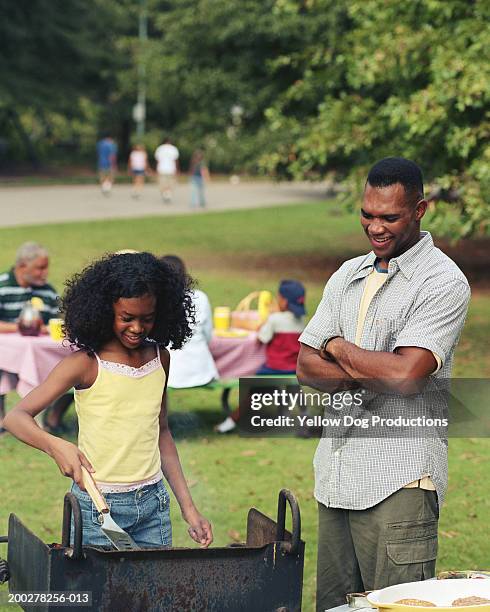 girl (11-13) grilling food at picnic, father watching - bbq family park imagens e fotografias de stock