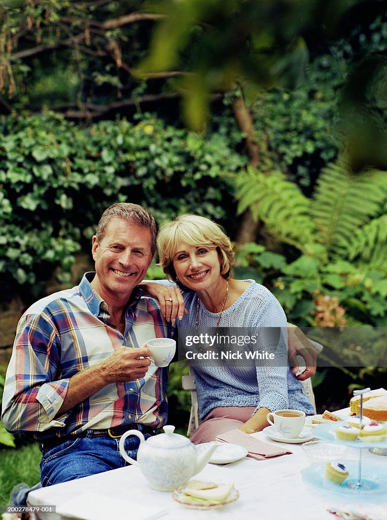 Couple having tea at garden table, smiling, portrait