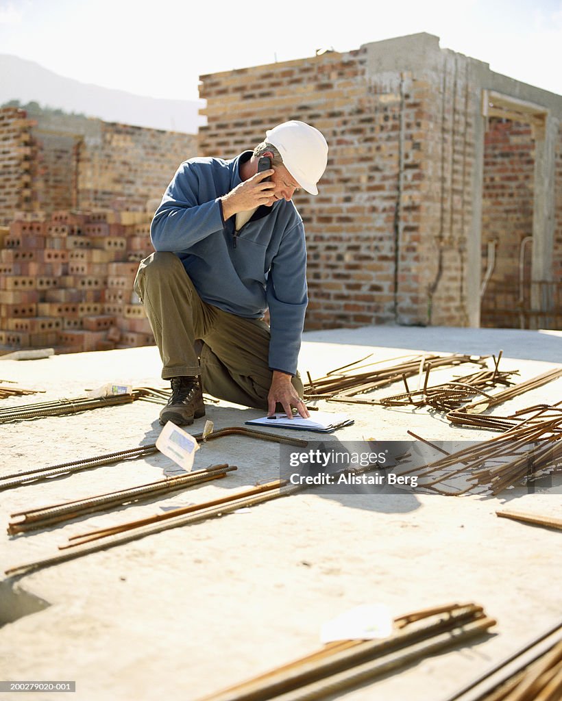 Builder in hard hat using mobile phone while looking at file
