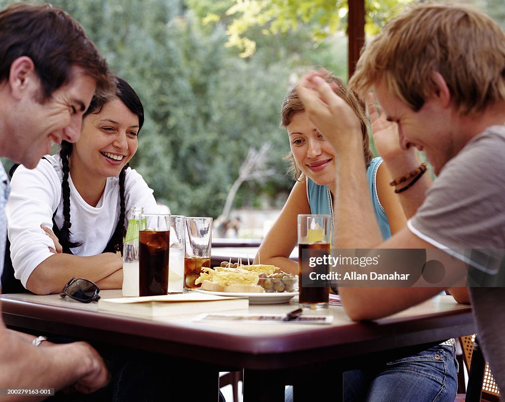 Two couples relaxing at outdoor cafe, smiling