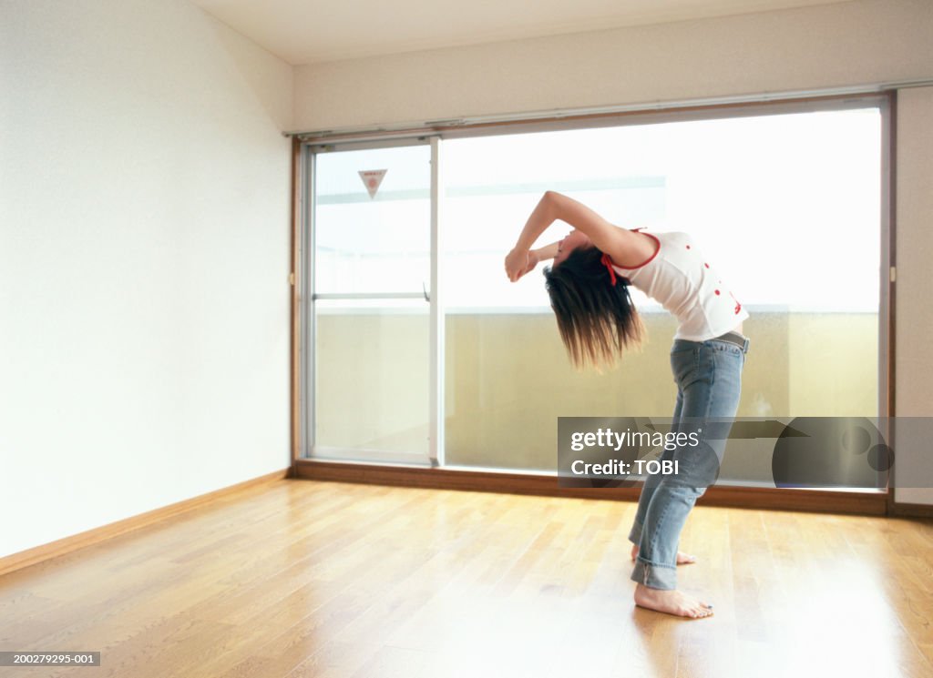 Young woman stretching in empty room, side view