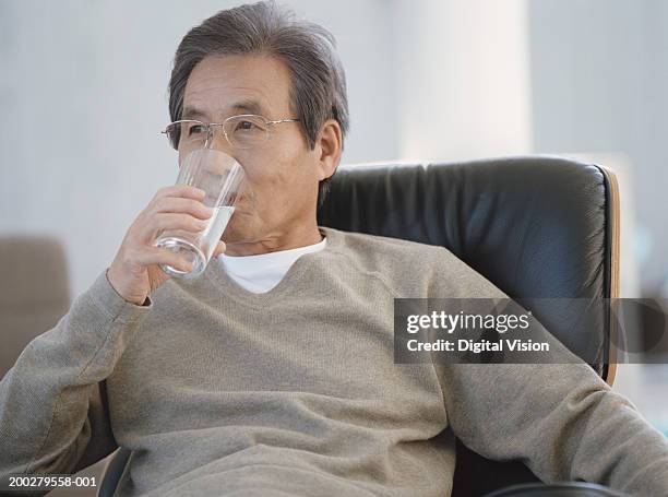 senior man sitting on armchair drinking glass of water - water glasses ストックフォトと画像