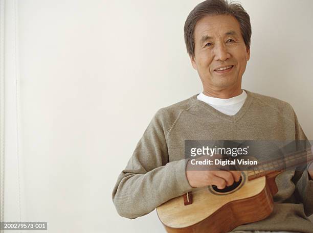 senior man playing ukelele indoors, smiling, portrait - ukulele stock-fotos und bilder