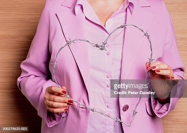 woman holding barbed wire in shape of heart, mid section - barb wire stock-fotos und bilder