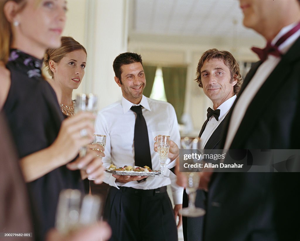Waiter by people wearing formal attire holding champagne glasses