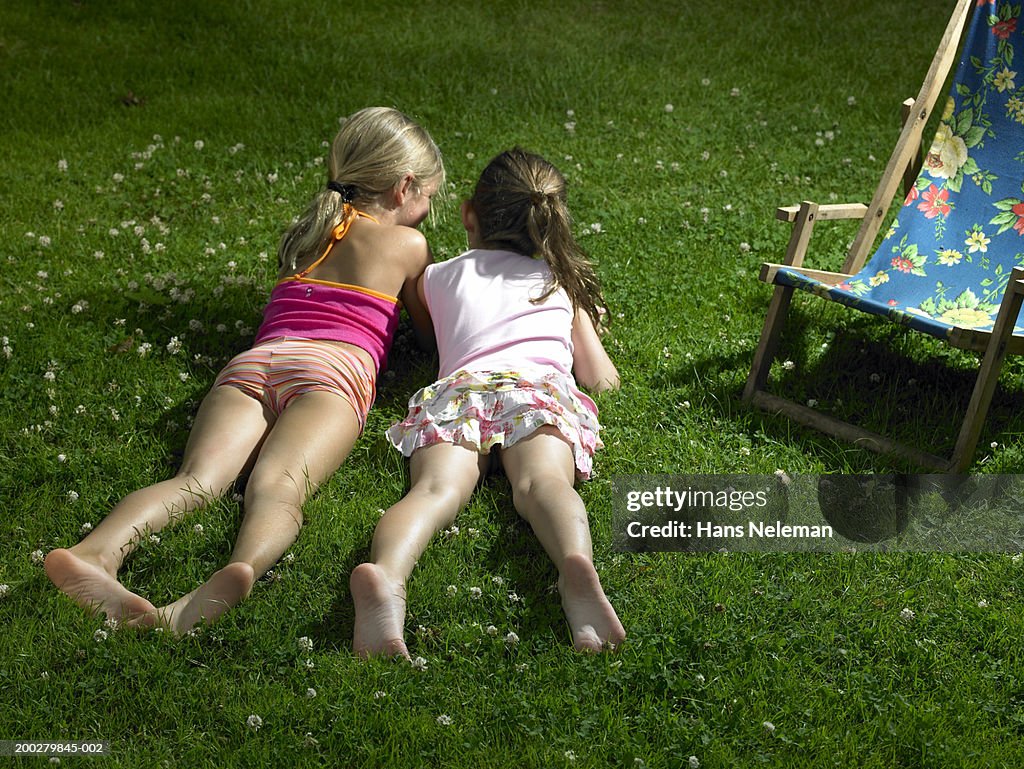 Two girls (4-6) lying in grass, talking, rear view