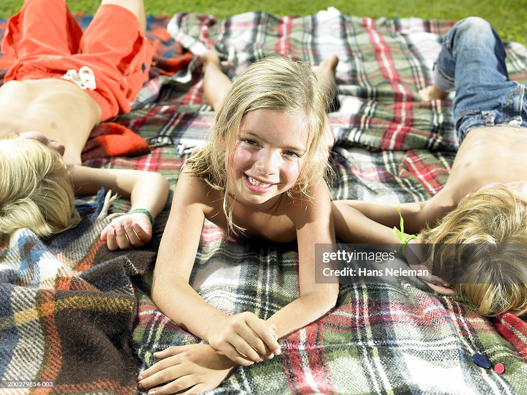 Girl (5-7) smiling on blanket in backyard, portrait