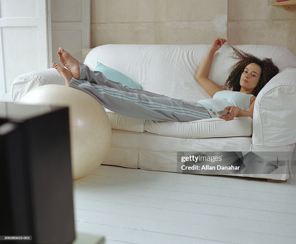 Woman lying on sofa using television remote control