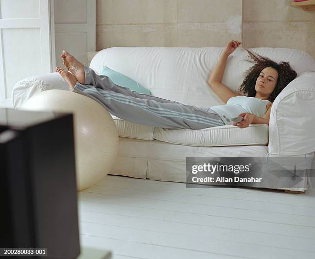 woman lying on sofa using television remote control - reclining stockfoto's en -beelden