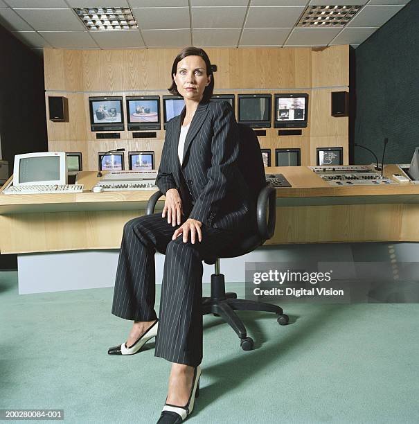 businesswoman sitting by desk, portrait, monitors on wall in background - hand on knee stock pictures, royalty-free photos & images