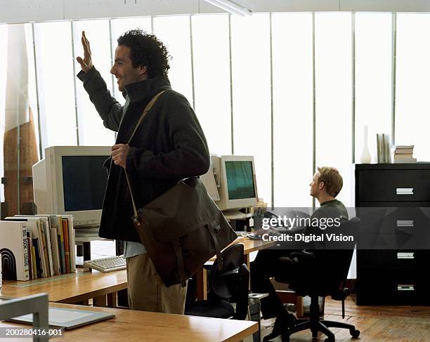 man standing in office carrying shoulder bag, hand raised - leaving office stock pictures, royalty-free photos & images