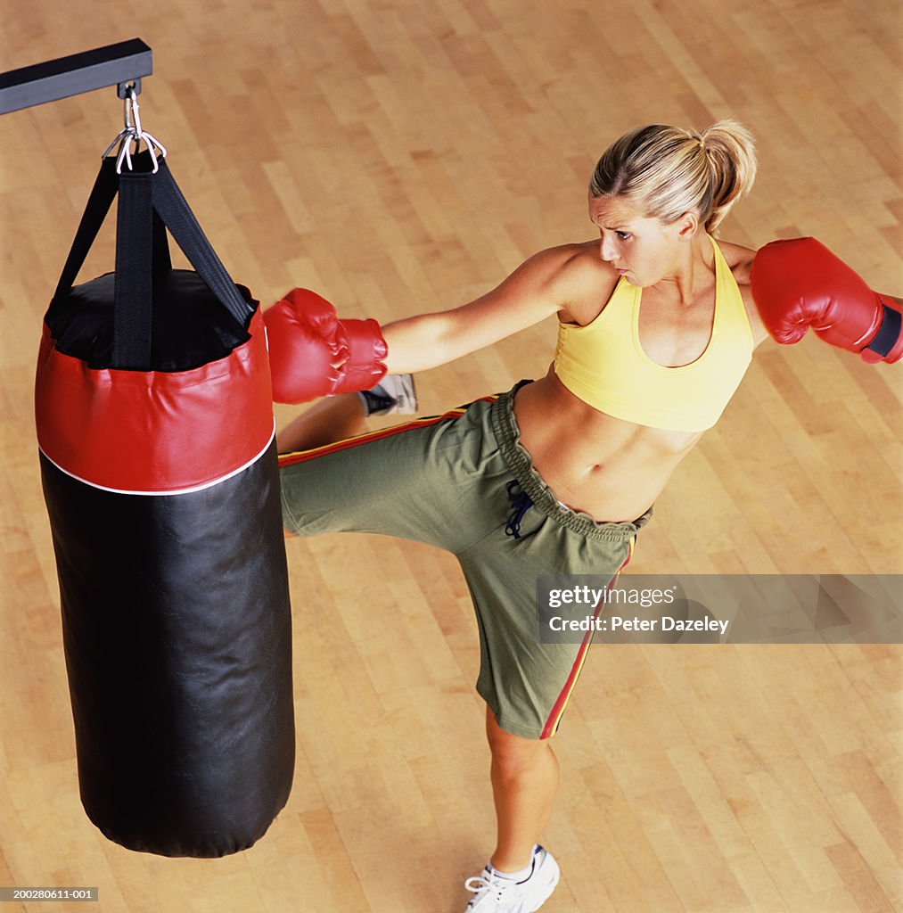 Young female boxer kicking punch bag
