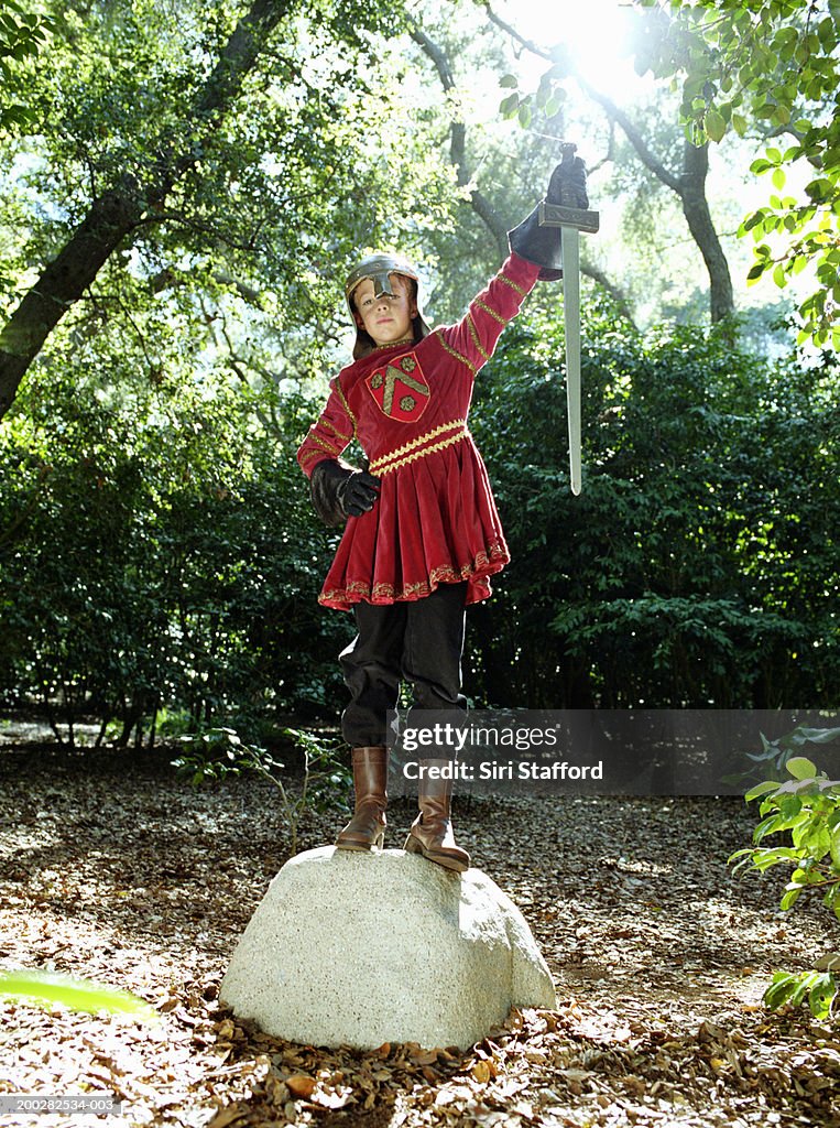 Boy (9-11) in Knight's costume standing on rock, holding sword