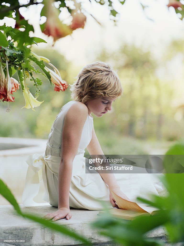 Girl (11-13) sitting on stone bench, reading book
