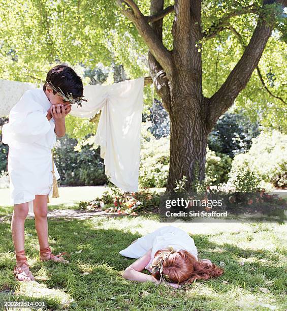 children (6-9) in costumes playing in garden - boy lying dead stockfoto's en -beelden