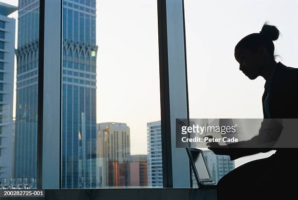 young woman using laptop by window in skyscraper, profile - arab woman silhouette stock pictures, royalty-free photos & images