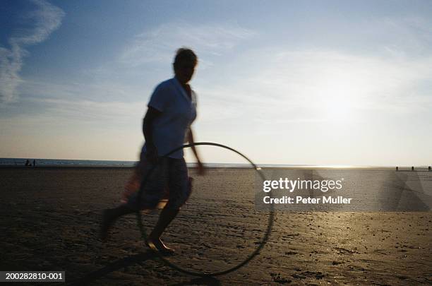 senior woman rolling hoop on beach (blurred motion) - hoop rolling stock pictures, royalty-free photos & images