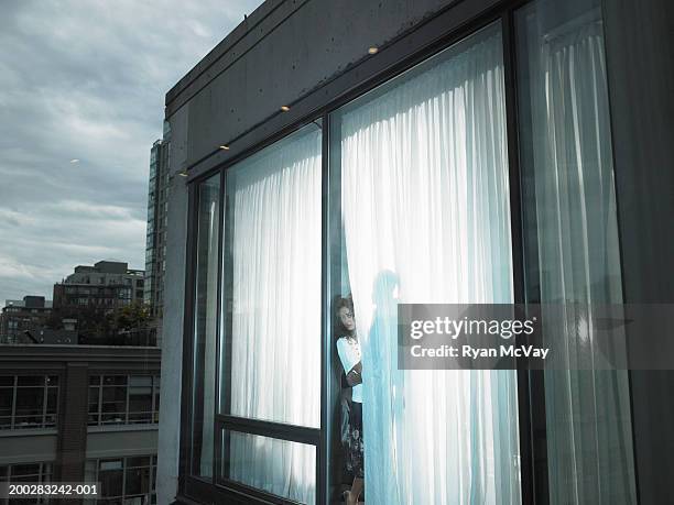 young couple beside window, woman peeking out from behind drapes - private view stockfoto's en -beelden