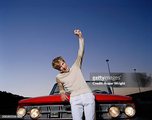 man leaning on bonnet of convertible car, arm raised, cheering - screaming happy in car stock-fotos und bilder