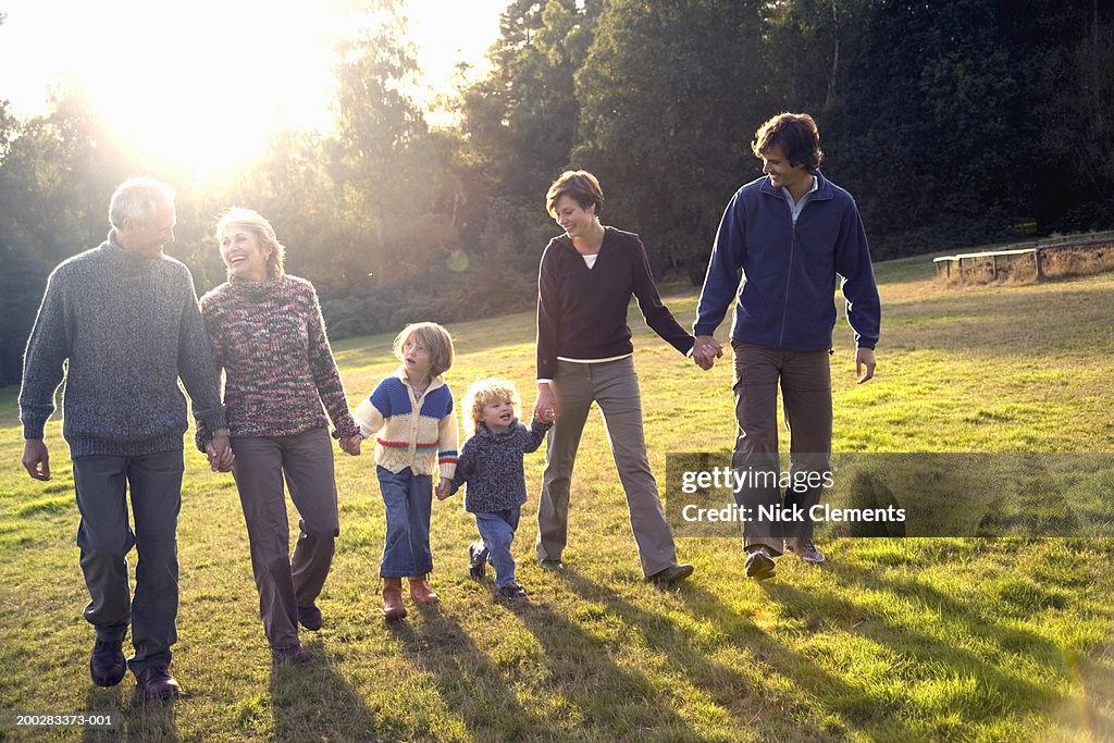 Three generational family walking hand in hand in park, smiling