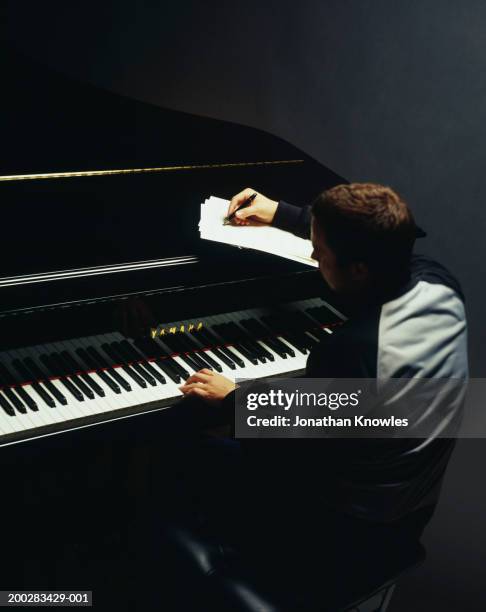 young man composing music at grand piano, rear view - writing instrument stock-fotos und bilder