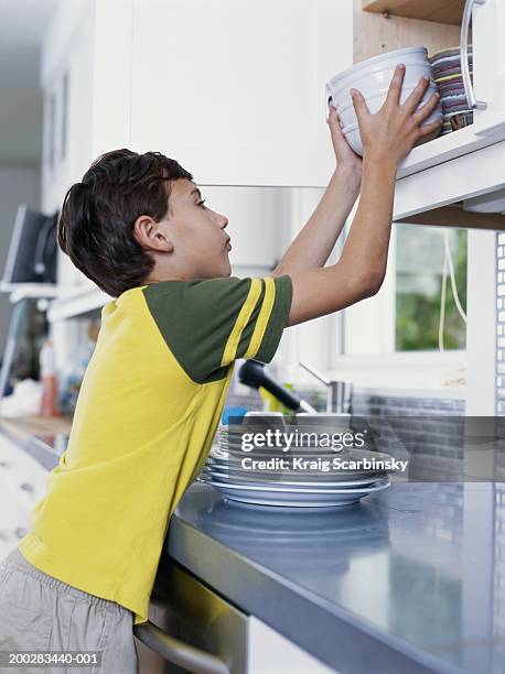boy (6-8) putting bowls away in kitchen cupboard, side view - plate side view stock pictures, royalty-free photos & images