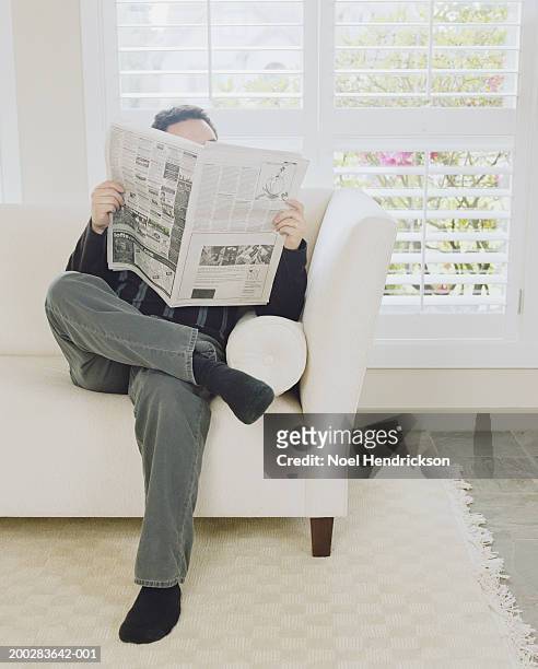man relaxing on sofa reading newspaper - viso nascosto foto e immagini stock