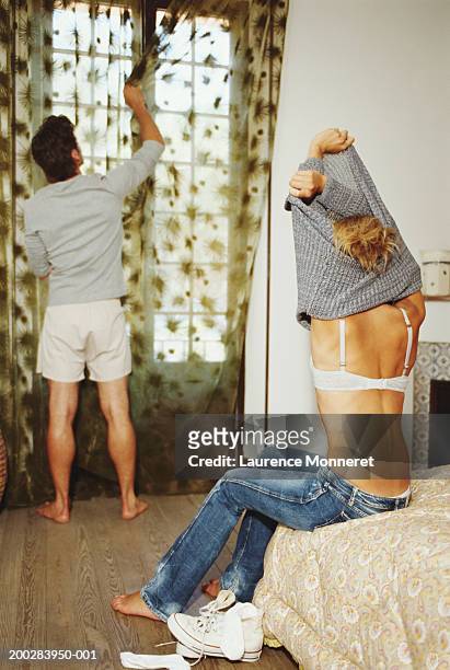 woman undressing on bed, man drawing curtains, rear veiw - entkleiden stock-fotos und bilder