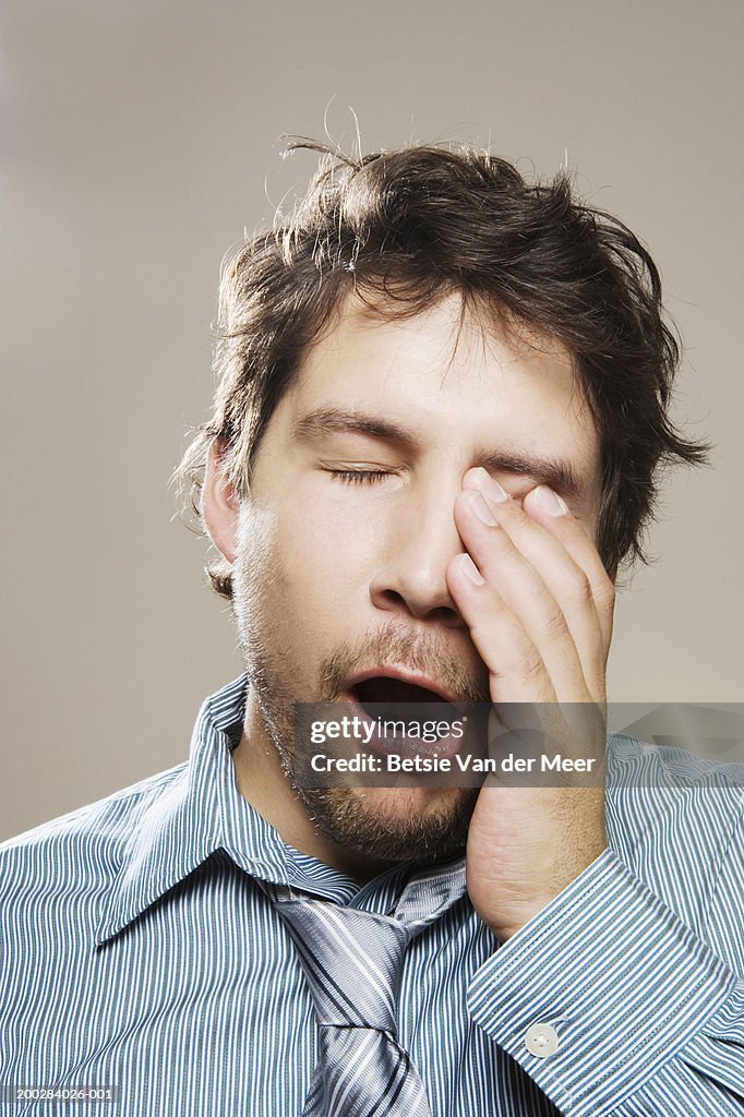 Man wearing shirt and loosened tie yawning, rubbing eye, close-up