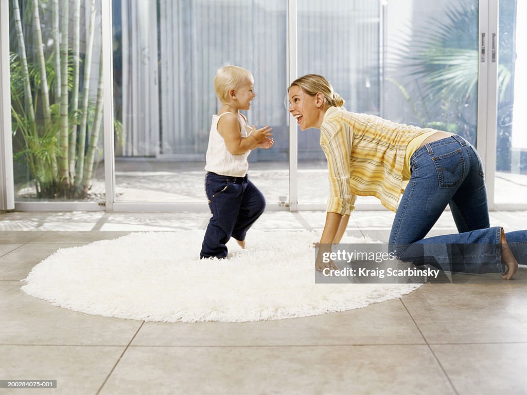 Woman crawling towards female toddler (21-24 months) on rug, side view