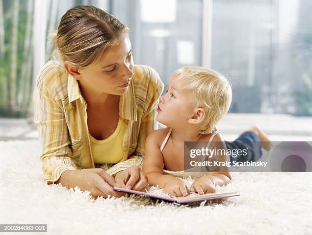 woman and female toddler (21-24 months) lying on rug with book, looking at each other - book sleeve stock pictures, royalty-free photos & images