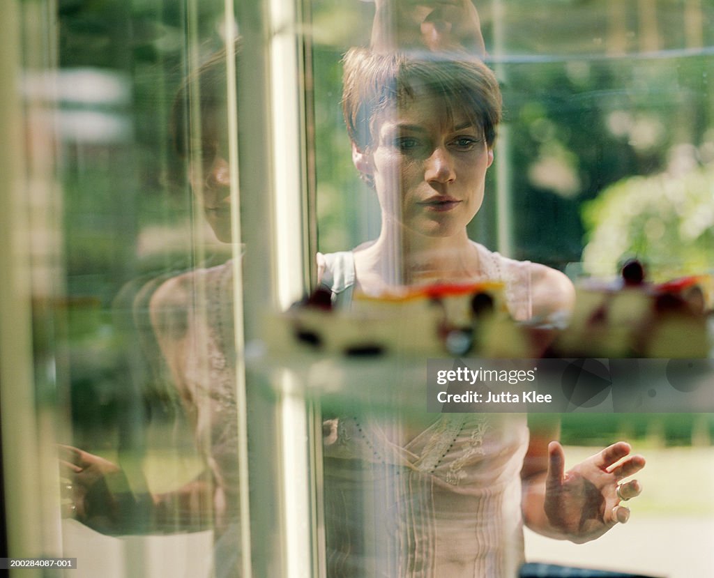 Woman looking at cake display in window, view through glass