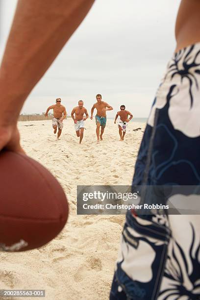 four men running towards man holding football on beach in foreground - fire eiland kustgebied stockfoto's en -beelden
