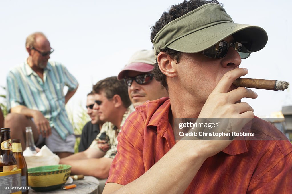 Man smoking cigar sitting with friends around table outdoors