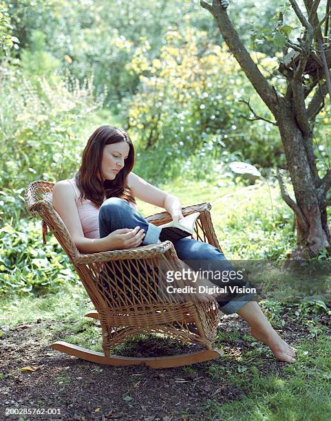 woman reading in garden, sitting on wicker rocking chair - rocking chair stockfoto's en -beelden