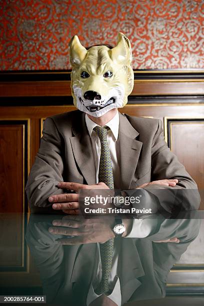 businessman sitting at boardroom table wearing mask of wolf's face - förklädnad bildbanksfoton och bilder