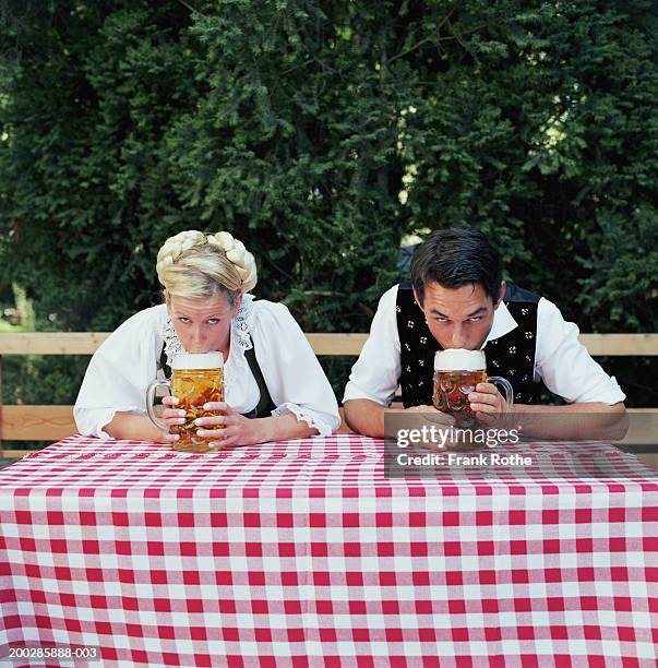 couple sitting at table drinking beer steins outdoors, portrait - camicetta a quadri foto e immagini stock