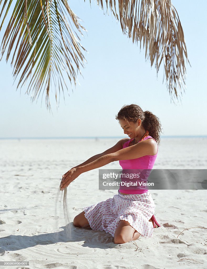 Woman playing with sand beneath palm tree (Palma sp.), smiling