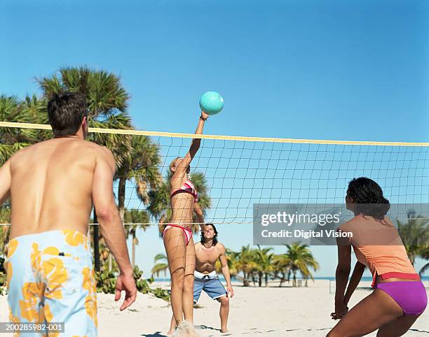 four people playing volleyball on beach - juego de voleibol de playa fotografías e imágenes de stock