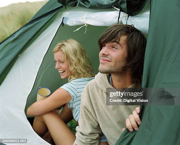 young couple sitting in tent opening, woman laughing (focus on man) - camping couple stockfoto's en -beelden