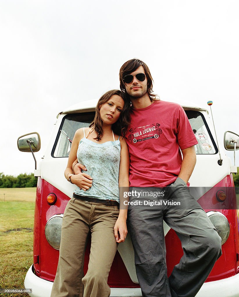 Young couple leaning against front of camper van, portrait