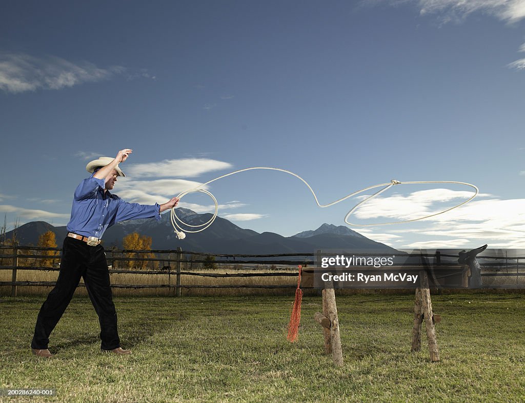 Young man lassoing sawhorse with cattle head on front, side view