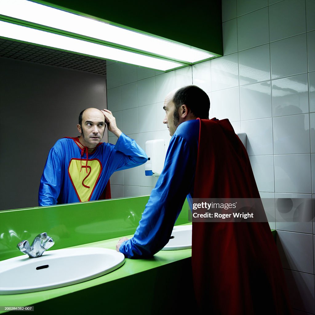 Man in superhero costume looking at reflection in mirror