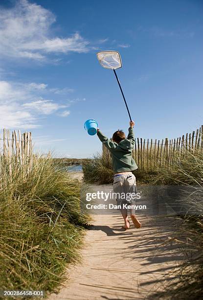 boy (4-6) holding up spade and fishing net by beach, rear view - boy barefoot rear view stockfoto's en -beelden